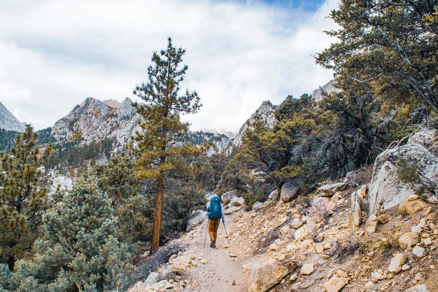 A man walking a mountain trail toward a horizon he can see